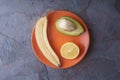 Avocado, lemon, banana halves lie on an orange plate on a slate Royalty Free Stock Photo