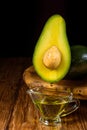 Avocado oil drops drain into a glass bowl. Avocado fruit and avocado oil on a wooden rustic tray on table Royalty Free Stock Photo