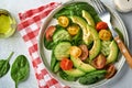 Avocado, red, yellow, black cherry tomato, spinach and cucumber fresh salad with spices pepper and olive oil in grey bowl on grey Royalty Free Stock Photo