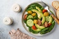 Avocado, red, yellow, black cherry tomato, spinach and cucumber fresh salad with spices pepper and olive oil in grey bowl on grey Royalty Free Stock Photo