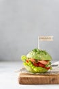 Avocado sandwich with green vegan burger, salted salmon, fresh vegetables and microgreen on wooden board on gray background. Side Royalty Free Stock Photo