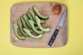 Avocado slices and core on cutting board with knife on yellow b