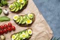 Avocado Summer Sandwich toast Recipe with guacamole, spinach, arugula and quail eggs on parchment paper on a concrete