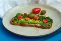 Avocado toast of rye bread with sauce, tomatoes, arugula on large grey plate on blue background. Vegetarian useful breakfast. Royalty Free Stock Photo