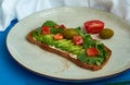 Avocado toast of rye bread with sauce, tomatoes, arugula on large grey plate on blue background. Vegetarian useful breakfast. Royalty Free Stock Photo