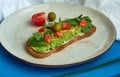 Avocado toast of rye bread with sauce, tomatoes, arugula on large grey plate on blue background. Vegetarian useful breakfast. Royalty Free Stock Photo