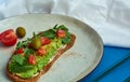 Avocado toast of rye bread with sauce, tomatoes, arugula on large grey plate on blue background. Vegetarian useful breakfast. Royalty Free Stock Photo