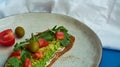 Avocado toast of rye bread with sauce, tomatoes, arugula on large grey plate on blue background. Vegetarian useful breakfast. Royalty Free Stock Photo