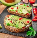 Avocado toasts - bread with avocado slices, pieces of red pepper and sesame on black stone board Royalty Free Stock Photo