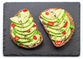 Avocado toasts - bread with avocado slices, pieces of red pepper and sesame on black stone board Royalty Free Stock Photo