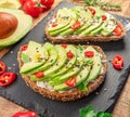 Avocado toasts - bread with avocado slices, pieces of red pepper and sesame on black stone board Royalty Free Stock Photo