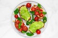 Avocado and tomatoes toasts with hummus, sesame and basil in a plate over white marble background. vegan food Royalty Free Stock Photo