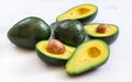 Avocados, whole and halved - seeds visible, on white working board