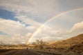 a road and mountain with a rainbow in the sky above