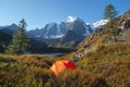 Awesome autumn camping in top of mountain. Lonely orange tent is hidden in a mountain forest among red dwarf birch bushes. Tourism