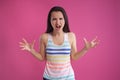 Brunette woman with long hair, dressed in colorful striped shirt, posing against pink studio background. Sincere