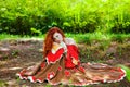 Awesome girl with freckles and red hair posing with a lowered red dress and bare shoulders on wild nature.