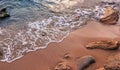 Awesome nature background. Soft beautiful ocean wave on sandy beach with rocks during sunset. Backdrop