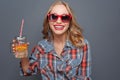 Awesome and nice girl is holding a cup with some juice and a piece of orange in it. She is laughing. Girl wears dark