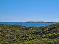 Awesome shot of a land with green bushes, a calm turquoise sea in background, a clear and blue sky