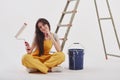 Awesome work with painting the walls. Beautiful brunette in yellow uniform and blue colored bucket sits near the ladder