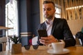 Awesome young businessman reading news on smartphone and drinking morning coffee from big white cup