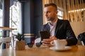 Awesome young businessman reading news on smartphone and drinking morning coffee from big white cup