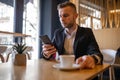 Awesome young businessman reading news on smartphone and drinking morning coffee from big white cup