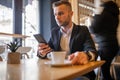 Awesome young businessman reading news on smartphone and drinking morning coffee from big white cup