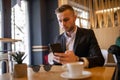 Awesome young guy or businessman reading news on smartphone and drinking morning coffee from big white cup