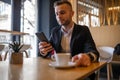 Awesome young guy or businessman reading news on smartphone and drinking morning coffee from big white cup