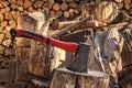 Ax stuck in a wooden deck against the background of sawn logs and woodpile Royalty Free Stock Photo