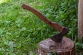 Axe driven into a stump in the yard against the background of green grass