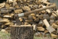 An axe stuck in a log in front of a pile of wood Royalty Free Stock Photo