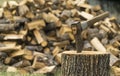 An axe stuck in a log in front of a pile of wood