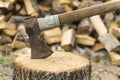 An axe stuck in a log in front of a pile of wood Royalty Free Stock Photo
