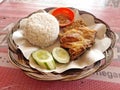 Ayam Penyet is Indonesian street food with savory fried chicken, rice and fried tempeh, cucumber and sambal