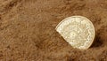 Golden aztec coin in sand.