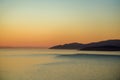 azure smooth surface of the ocean with yellow glare of the setting sun, black silhouettes of mountains