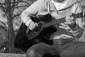 B&W - Young man sitting on wooden chair in park and playing guitar Royalty Free Stock Photo