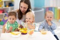 Babies having lunch in kindergarten. Kids eat healthy food in creche. Carer with children sitting at dinner table in