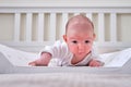 A baby aged 1 month learns to keep his head lying on his stomach. Caucasian boy child in a home white bedroom