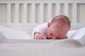 A baby aged 1 month learns to keep his head lying on his stomach. Caucasian boy child in a home white bedroom