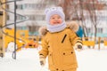 A baby aged 12-17 months on the playground in winter. The kid in the yellow jacket smiles sweetly, close up