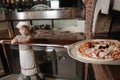 Baby baker puts pizza into the wood-burning stove