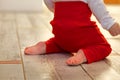 A baby in beautiful red pants with bare legs is kneeling on parquet floor Royalty Free Stock Photo