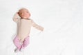 Baby in beige bodysuit and pink tights lies on white sheet Royalty Free Stock Photo