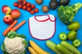 Baby bib surrounded by vegetables and fruits on blue background. Concept of healthy eating and first feeding of children, baby Royalty Free Stock Photo