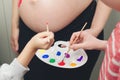 Baby birth expecting time and belly painting. Happy kids painting pregnant belly their mother Royalty Free Stock Photo