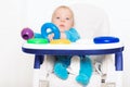 A baby with blue eyes holds his toys in his hands. A blond boy is sitting in his chair, playing with rings from the pyramid Royalty Free Stock Photo